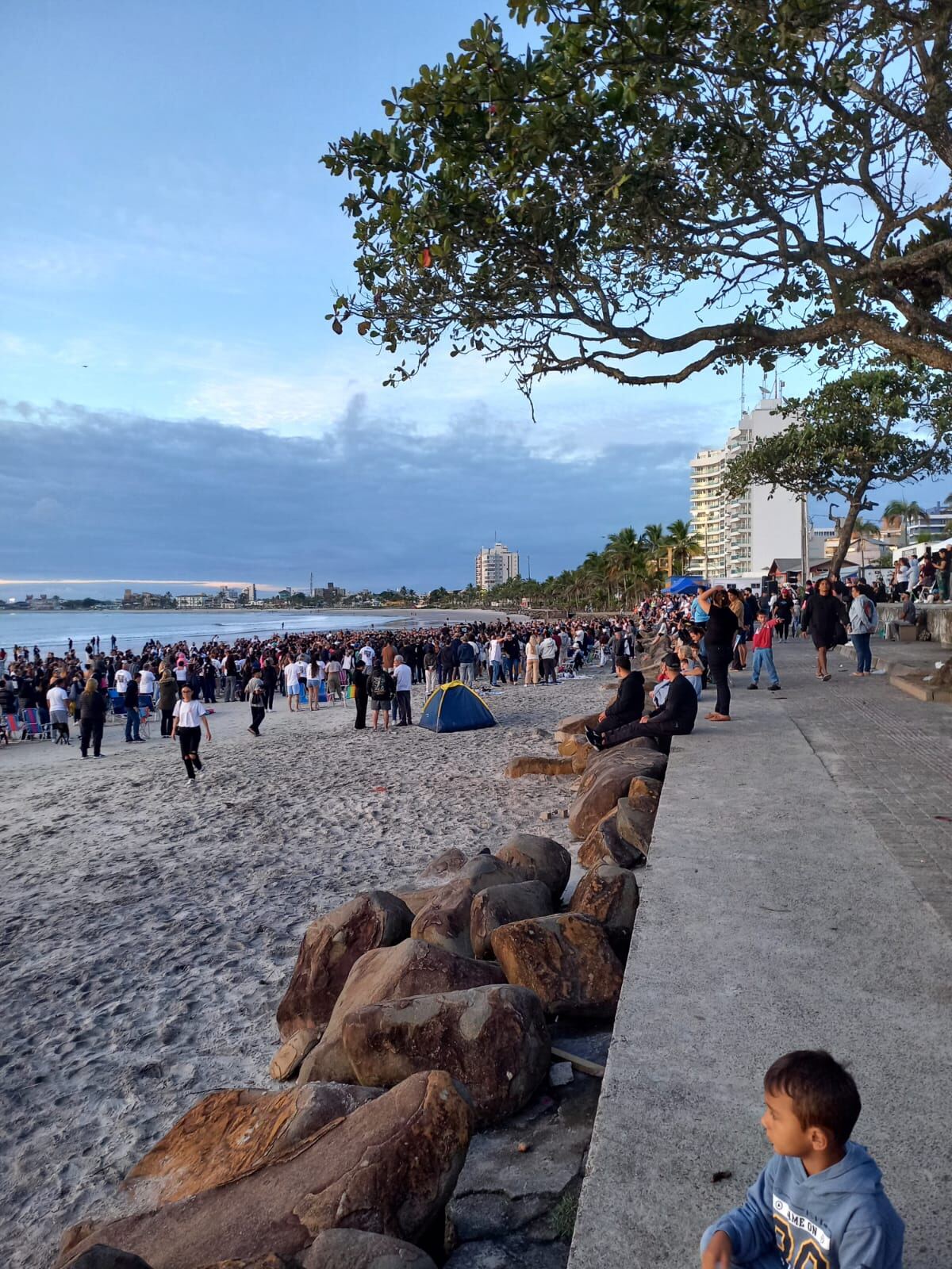 Vista lateral da orla com os participantes reunidos em oração