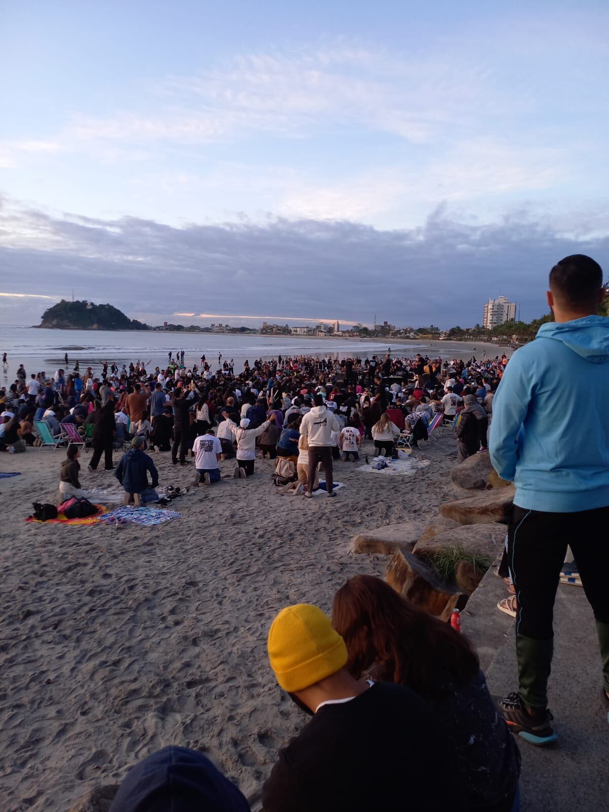 Participantes ajoelhados e com mãos levantadas durante o culto na praia